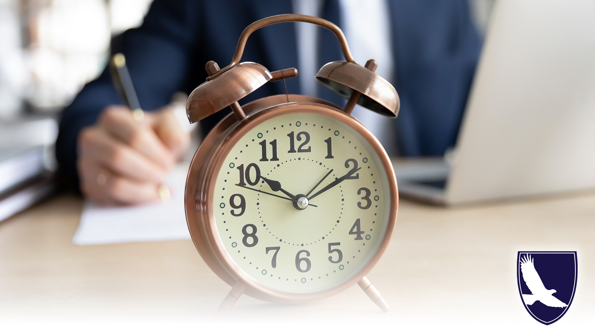Focus on clock standing on table with busy young businessman entrepreneur in formal wear on background, focused millennial male manager involved in casual working process, clock on desk